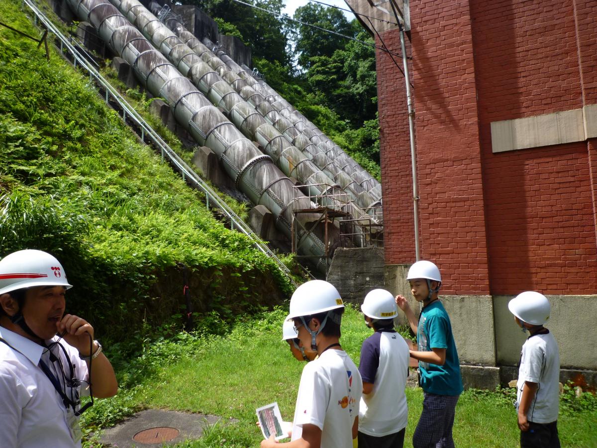 猪苗代町の水力発電所で巨大な水圧鉄管を眺める児童たち