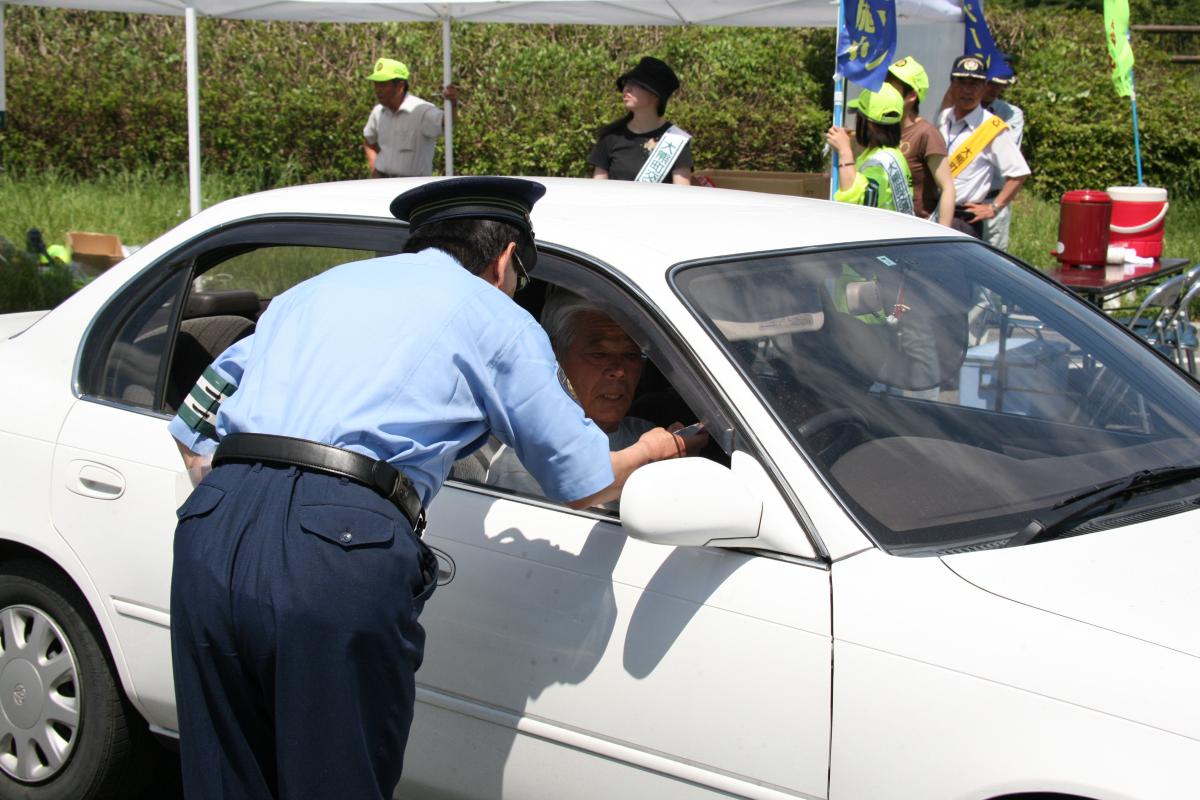 ドライバーに交通安全マスコットやチラシを渡して交通事故防止を呼び掛ける警察官