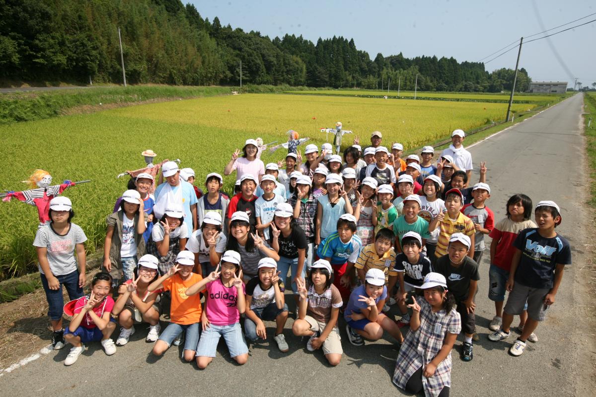 春にみんなで田植えし黄色く実った稲、案山子と共に記念写真に収まる5年生
