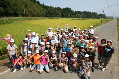 春にみんなで田植えし黄色く実った稲、案山子と共に記念写真に収まる5年生