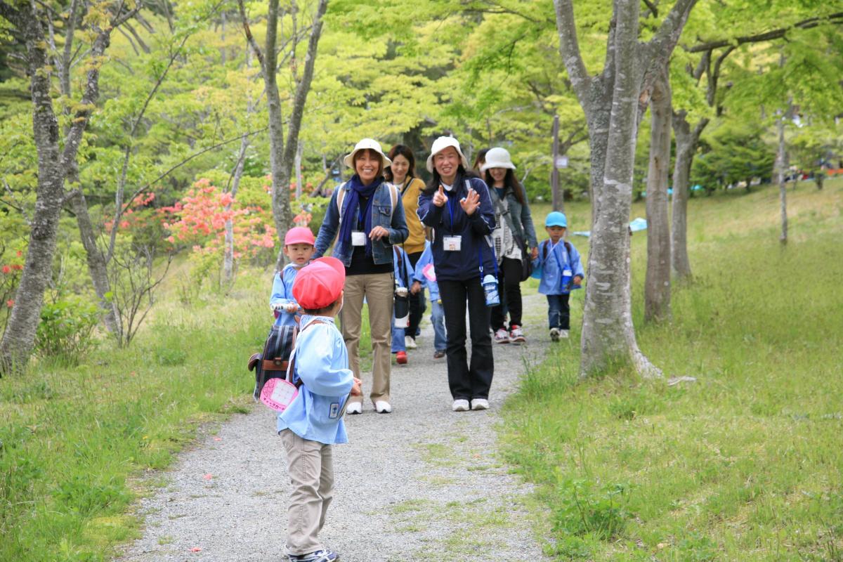 青葉若葉の光の中を笑顔で歩く親子たち