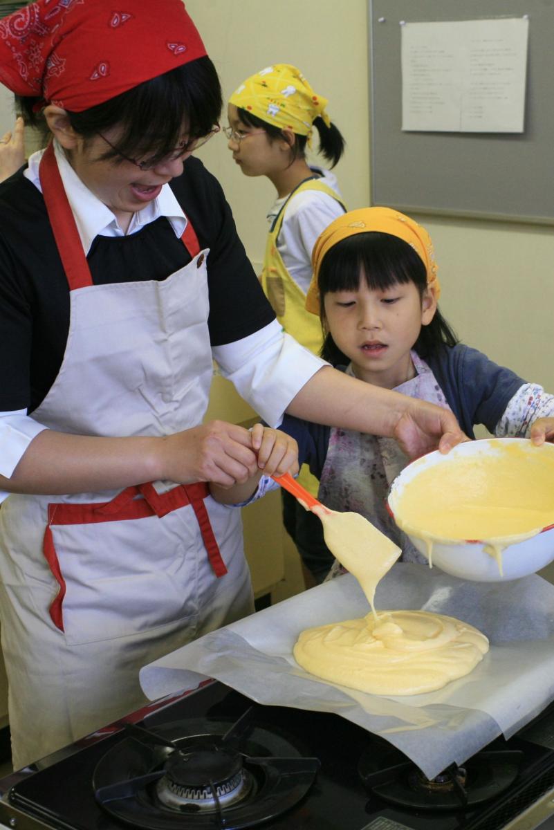 二人で協力してロールケーキの生地を天板に流し込む親子