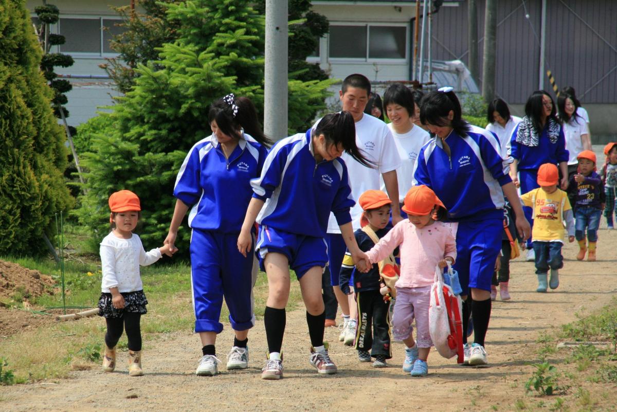 高校生のお兄さんお姉さんと手をつないでさつまいも畑のある双葉翔陽高校農場に向かう園児たち