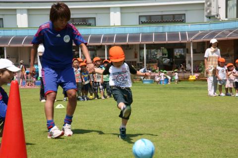 マリーゼの選手と手をつなぎドリブルの練習をする園児