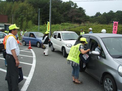 国道を走行するドライバーにエコバッグと交通安全母の会手作りのマスコットを手渡す参加者