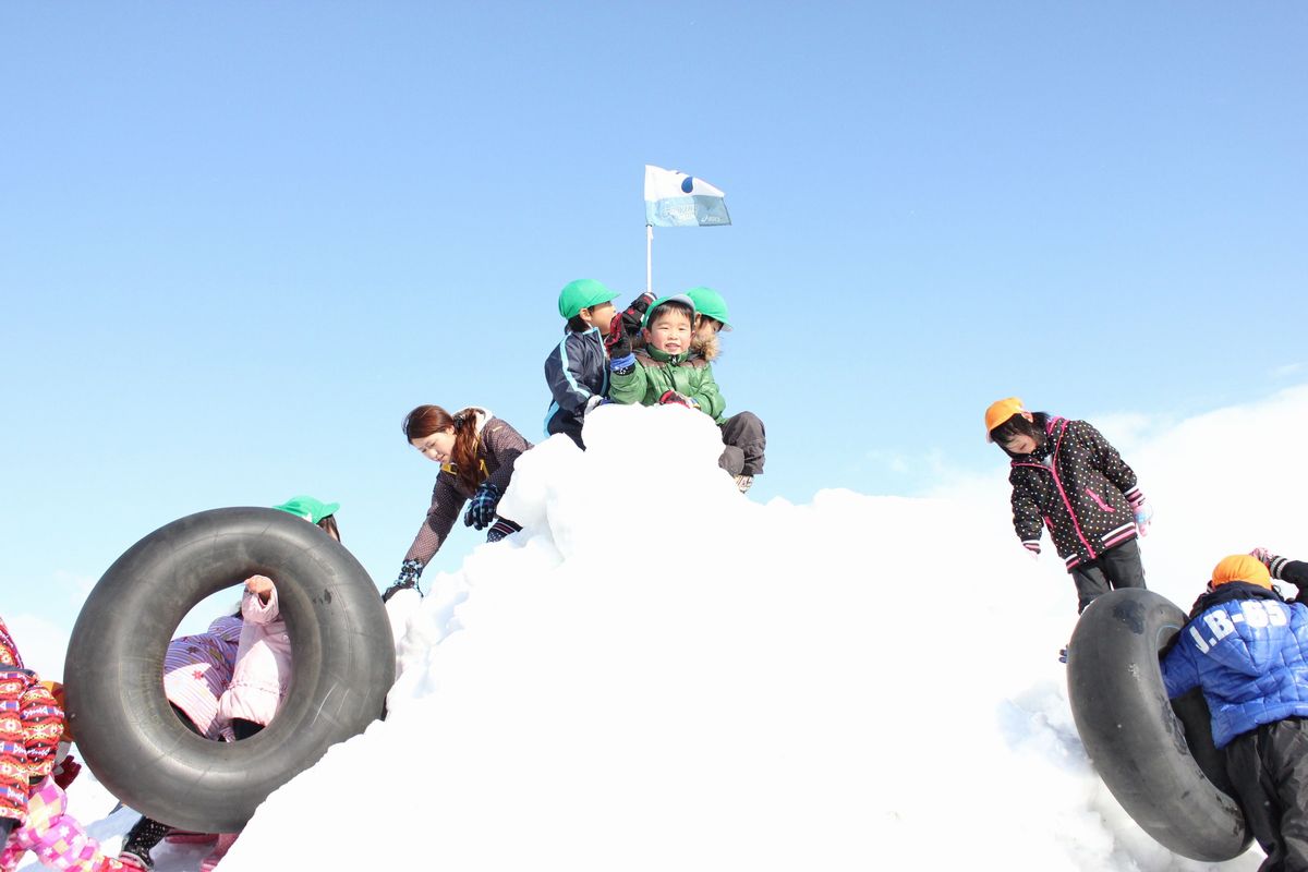 雪山の頂上に登り旗を掲げる園児