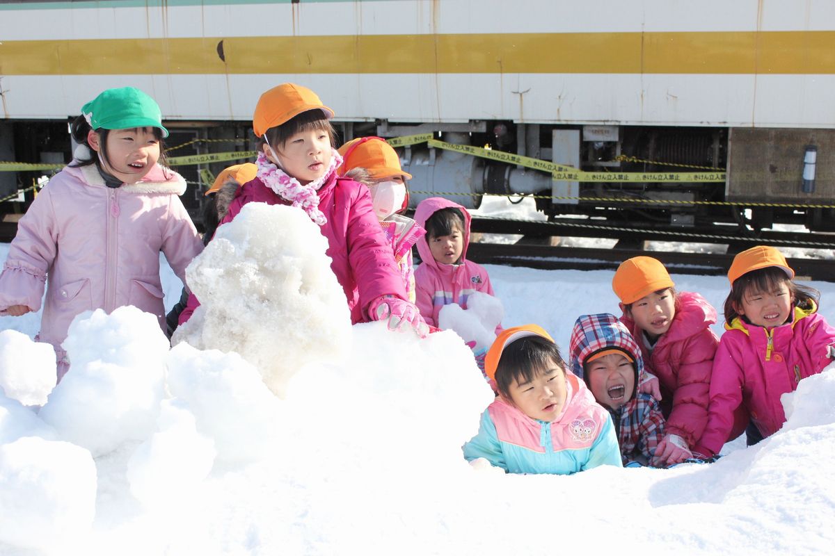 おおきな小法師の雪像に顔を描くのを嬉しそうに見つめる園児たち