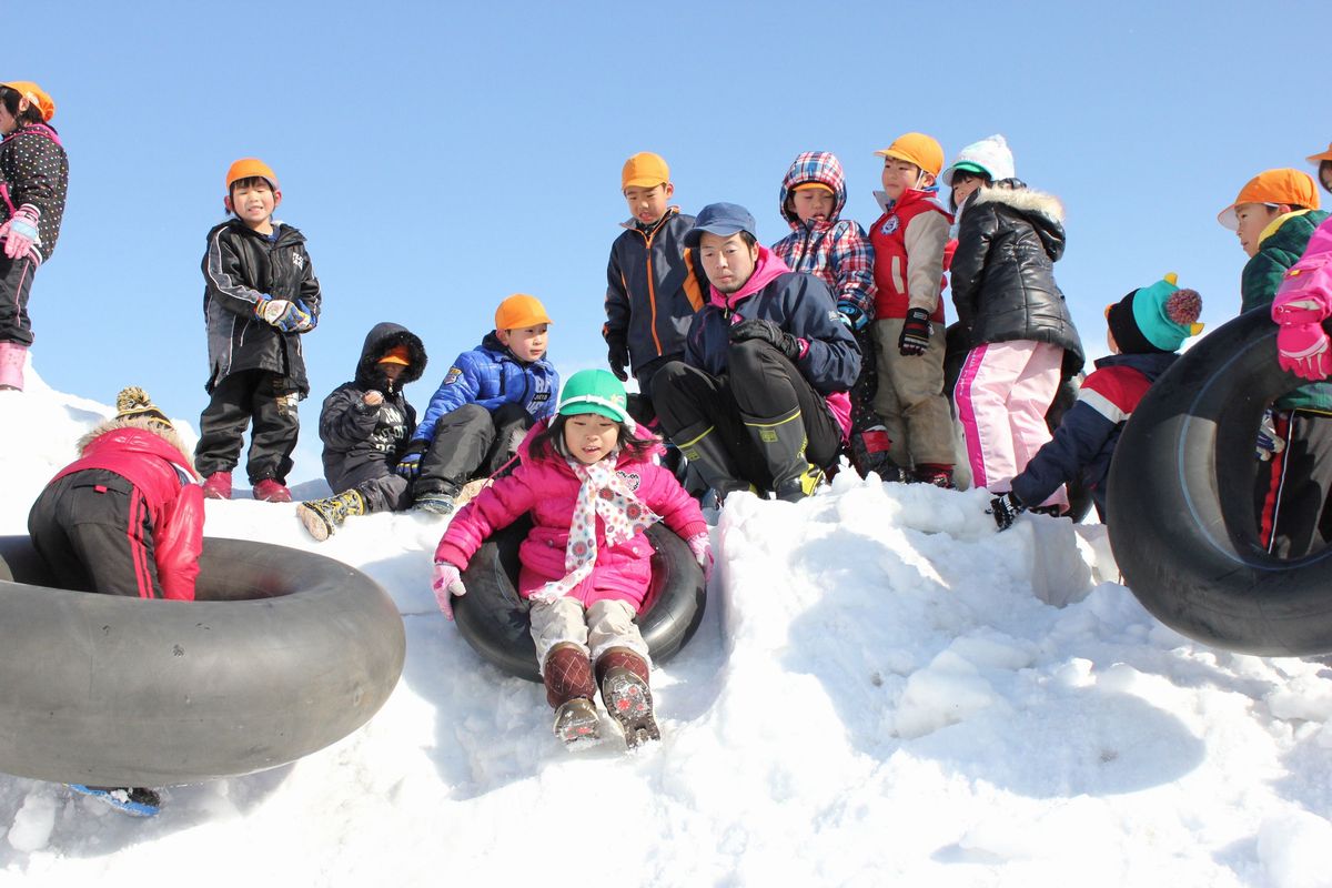雪の山をゴムチューブで滑り降りて楽しむ園児たち