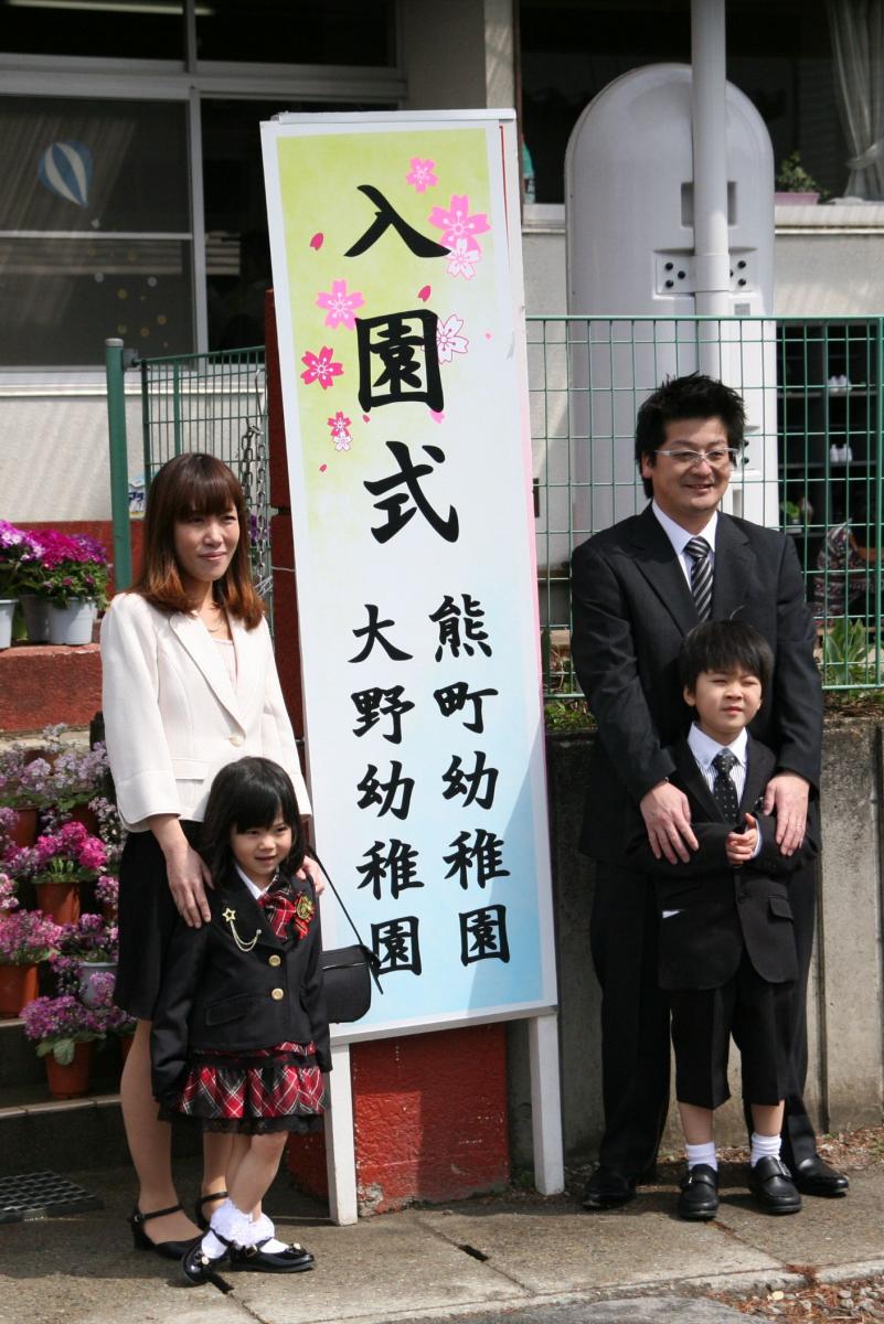入園式の立て看板の前で記念撮影する新入園児の家族
