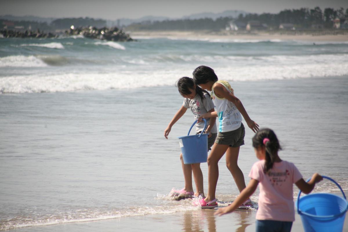 バケツを持って嬉しそうに海に足をつける参加児童