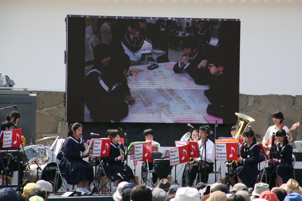 大きなモニターに学校生活が映し出される中、演奏を披露する吹奏楽部