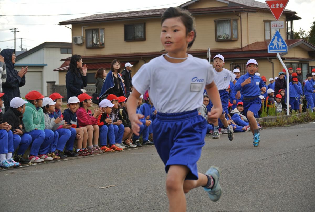 懸命に走る児童と、それを応援する保護者の方、上級生、下級生たち
