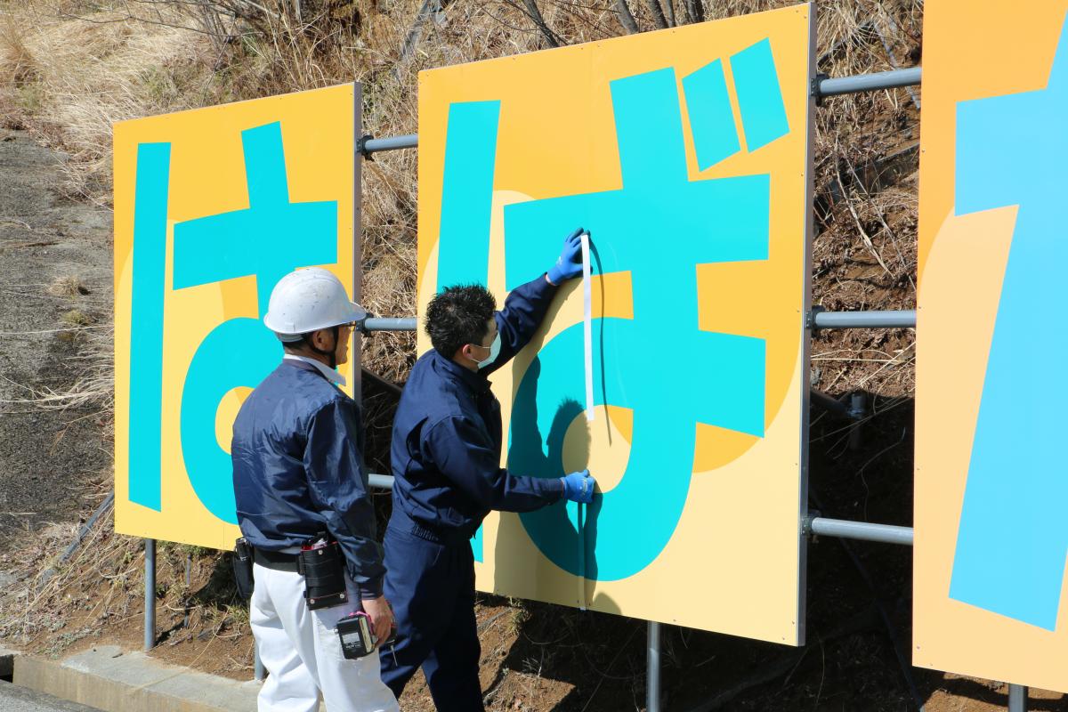 一時帰宅や除染作業などで町内に立ち入る方たちを元気づけたいと思いを込めて大熊中生が考案した「はばたけ新大熊町開幕」の看板