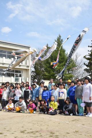 校庭に掲げられたこいのぼりと記念撮影をする室井市長、県電設業協会の方、児童ら