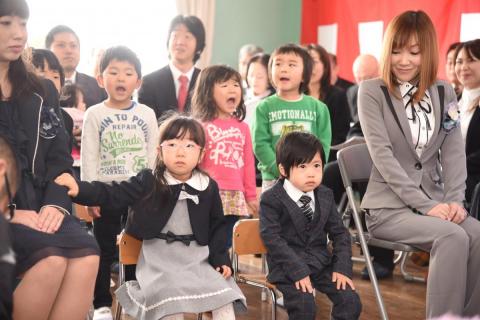 在園児のお兄さん、お姉さんが披露する園歌に興味深々で聞き入る新入園児の2人