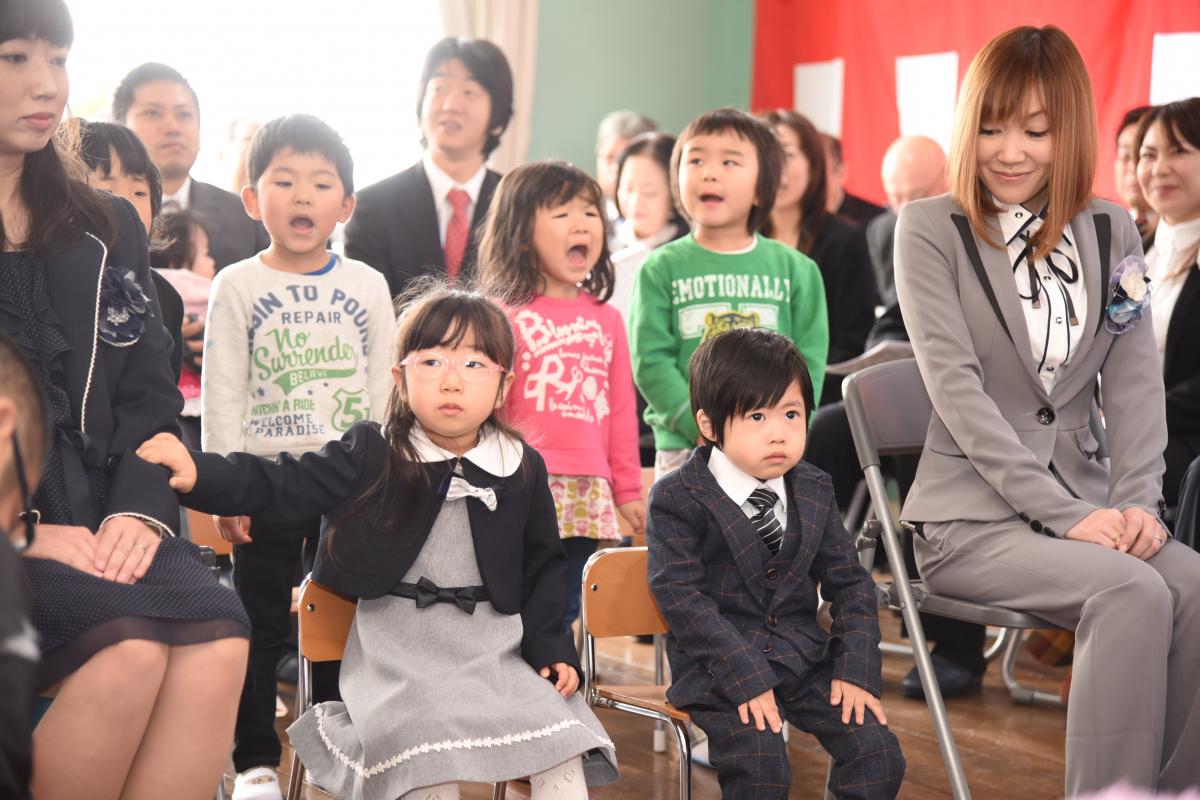 在園児のお兄さん、お姉さんが披露する園歌に興味深々で聞き入る新入園児の2人