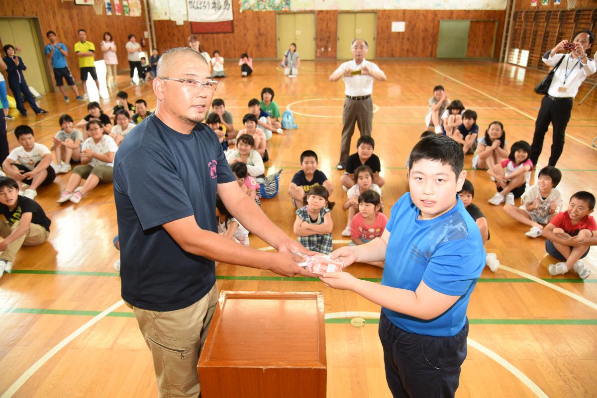 大熊町出身で、現在は福岡県筑後市でイチゴ栽培をしている農家の北原さんからアイスを手渡される児童の代表