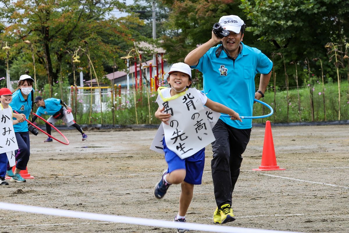 背の高い男の先生を見つけ、ゴールまで走る児童