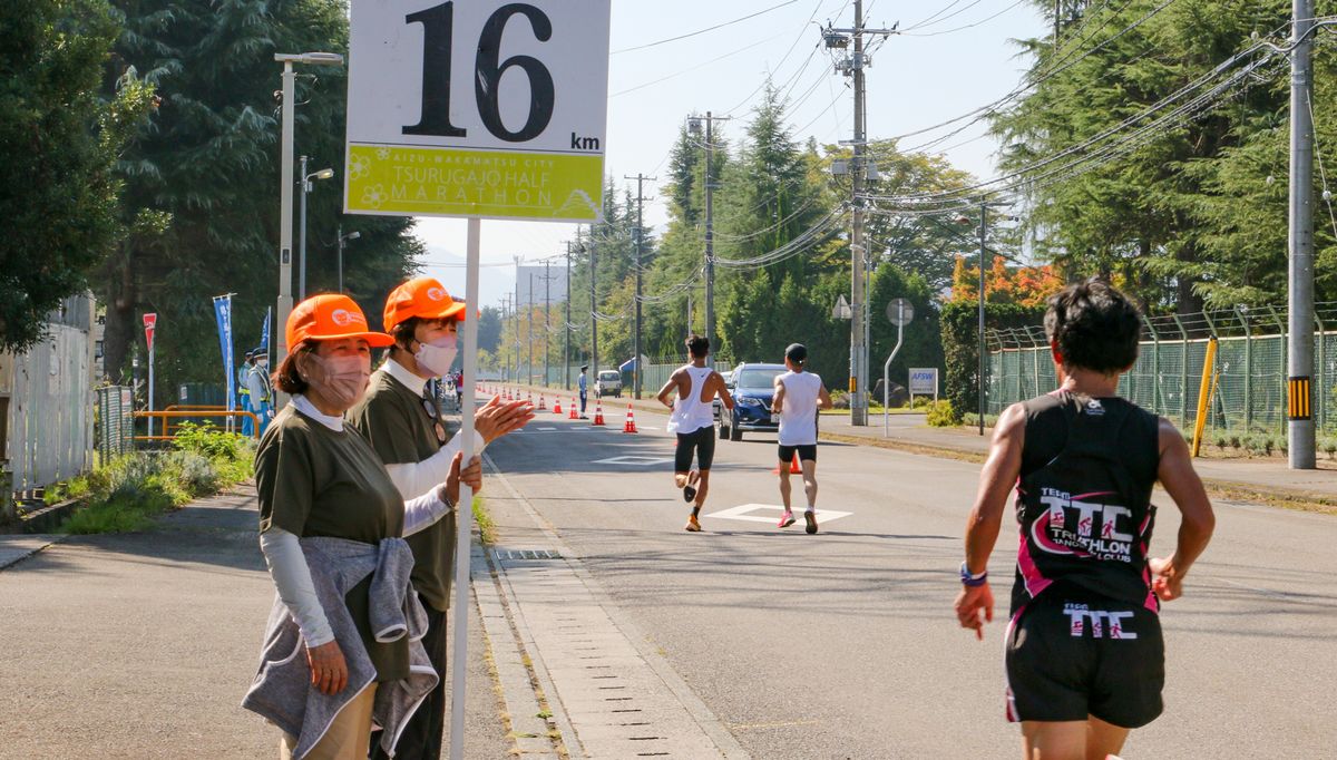 距離表示のプラカードを掲げるボランティアの町民