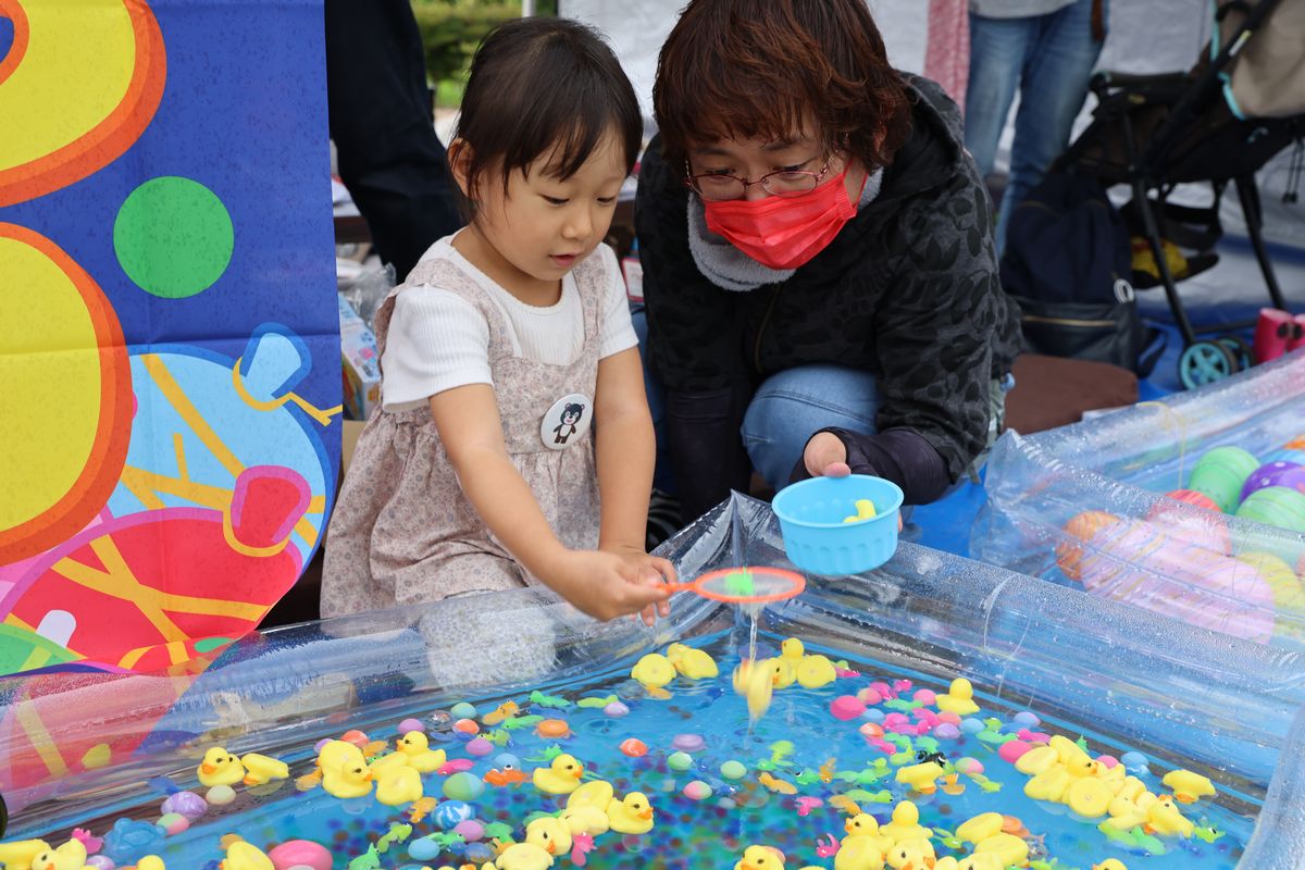 あひる、金魚、スーパーボール、色とりどりのおもちゃを前にどれにしようか迷いながらすくい上げる子ども。