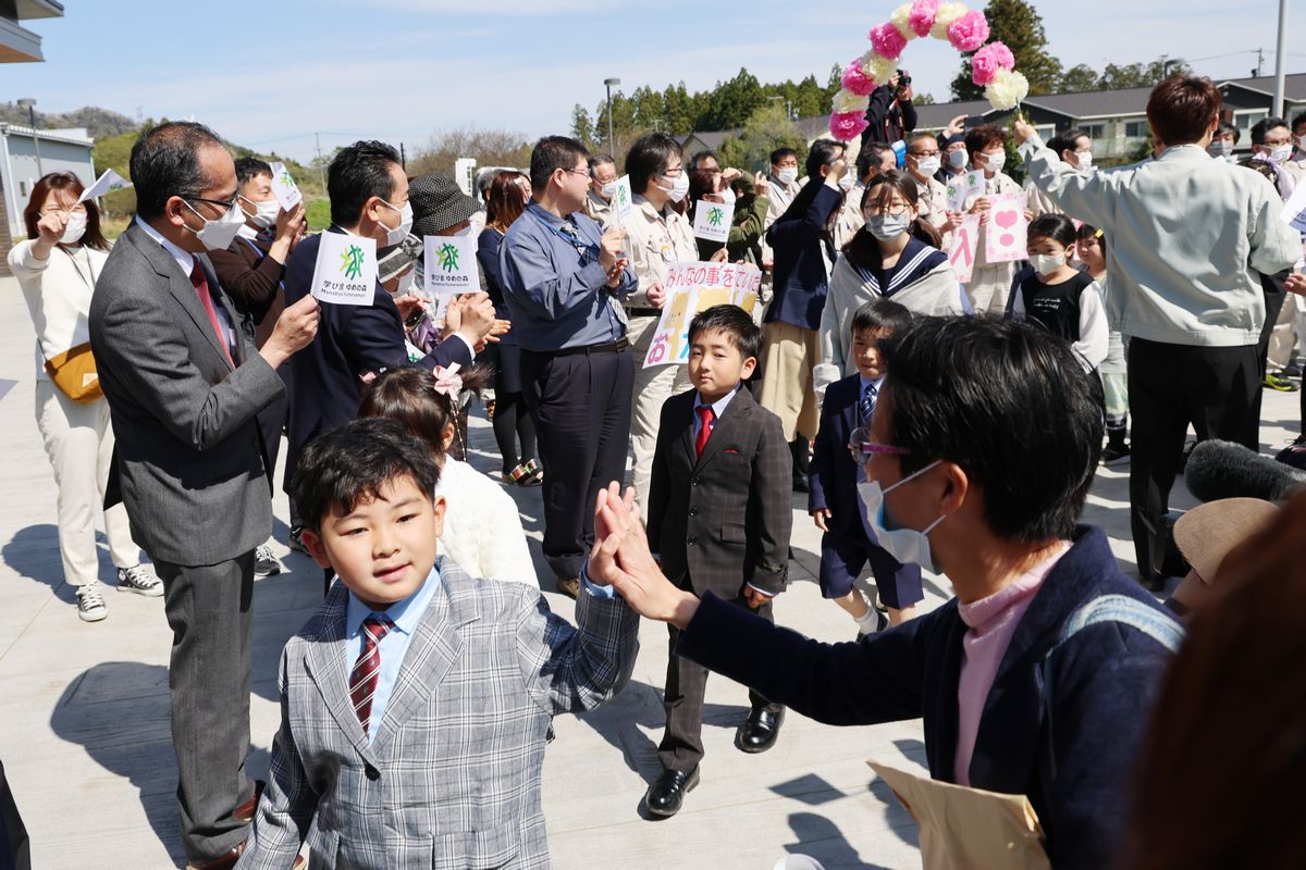 式に先立ち、会場前の広場で「みんなでお出迎えセレモニー」が開かれました。町民ら約200人が会場までの通り道に並び、拍手をしたり、手旗を振ったりして子どもたちを歓迎。出迎えを受けた子どもたちは緊張しながらも笑顔で応えながら会場までの花道を歩みました。