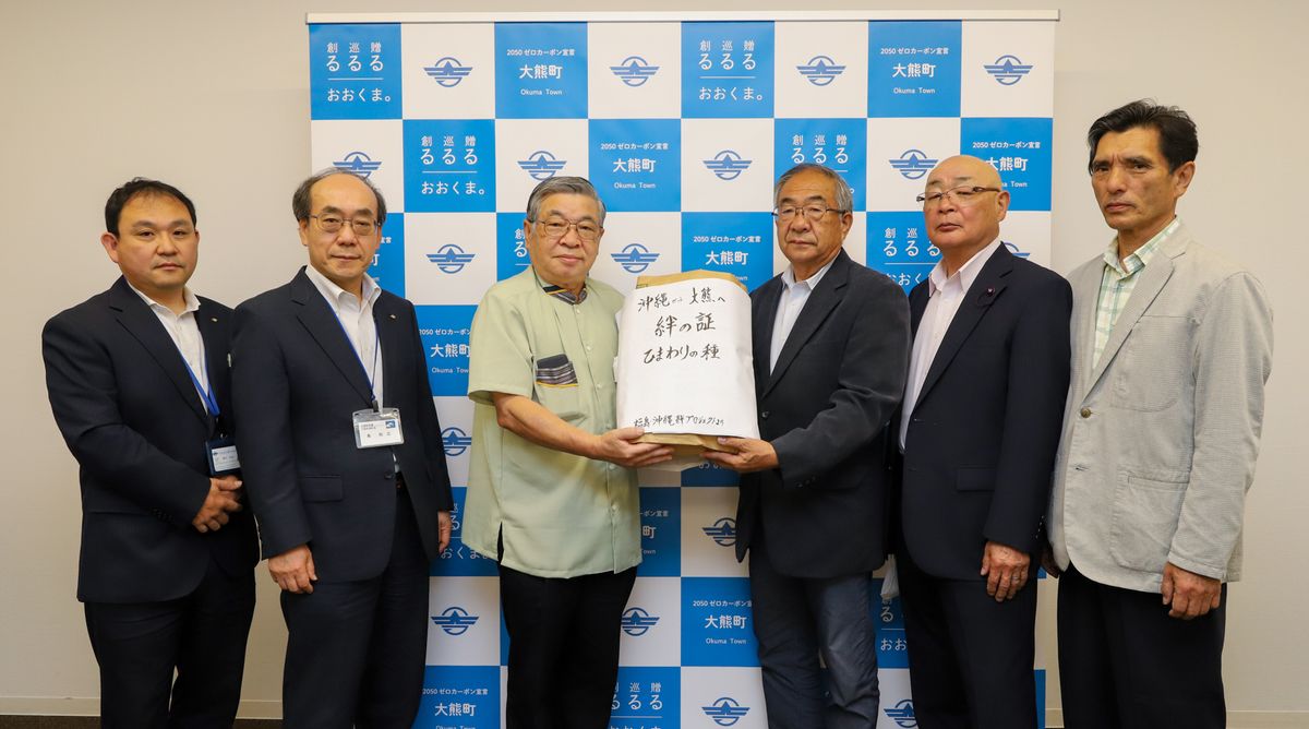 鈴木副理事長から種を受け取る渡部会長（右から3人目）