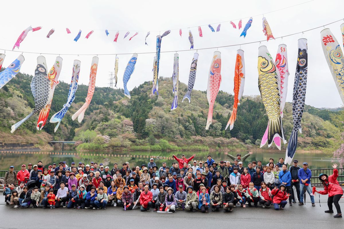 おおくまコミュニティづくり実行委員会は4月8日、町内大川原地区で春の坂下ダムウォーキングイベントを開きました。参加者した町民ら約200人は、大熊町交流ゾーン「linkる大熊」前広場を出発し、坂下ダム施設管理事務所前に到着すると恒例の記念撮影を行い、その後、特別に開放されたダム堤体を通ってダム湖を一周しました。