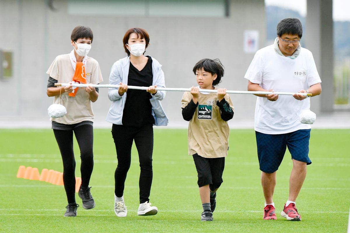 子どもたちが考えた9種類の競技を参加者全員で競い合う「ゆめりんピック」。さまざまな競技にチャレンジしながらチームでつないでいきます。写真は最初の競技「台風の目」。棒の両端にぶら下げられた球を落とさないように四人で竿を持って走り抜けます。