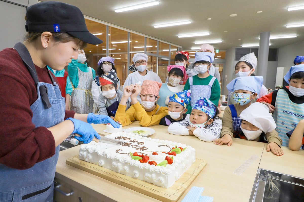 池田さん（写真左）が用意した開校を祝う特大ケーキが披露されると、子どもたちから歓声が上がりました。