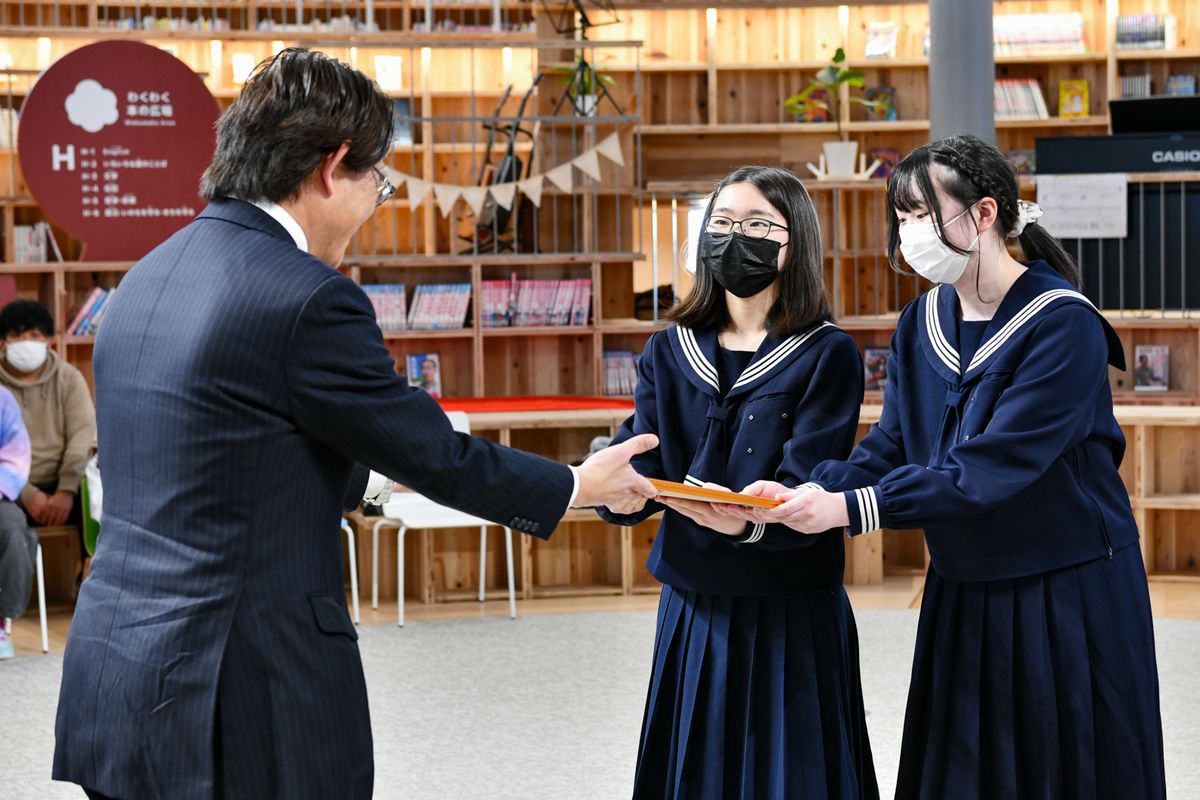 ワンアースの長谷川洋一代表（左）から宇宙桜の証である宇宙フライト証明書を受け取る卒業生。