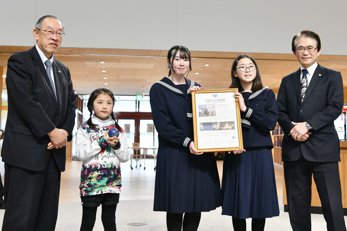 ワンアースの長谷川洋一代表（右）と甚野源次郎顧問（左）から3人へ宇宙桜の証である宇宙フライト証明書と地球をイメージした直径約5センチのラピスラズリの玉「紲石（きずないし）」が手渡されました。