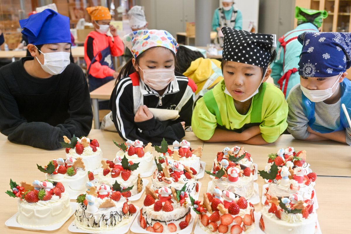 クリームやチョコレート、サンタクロースや雪だるまの菓子で飾り付けられたケーキを見つめる子どもたち