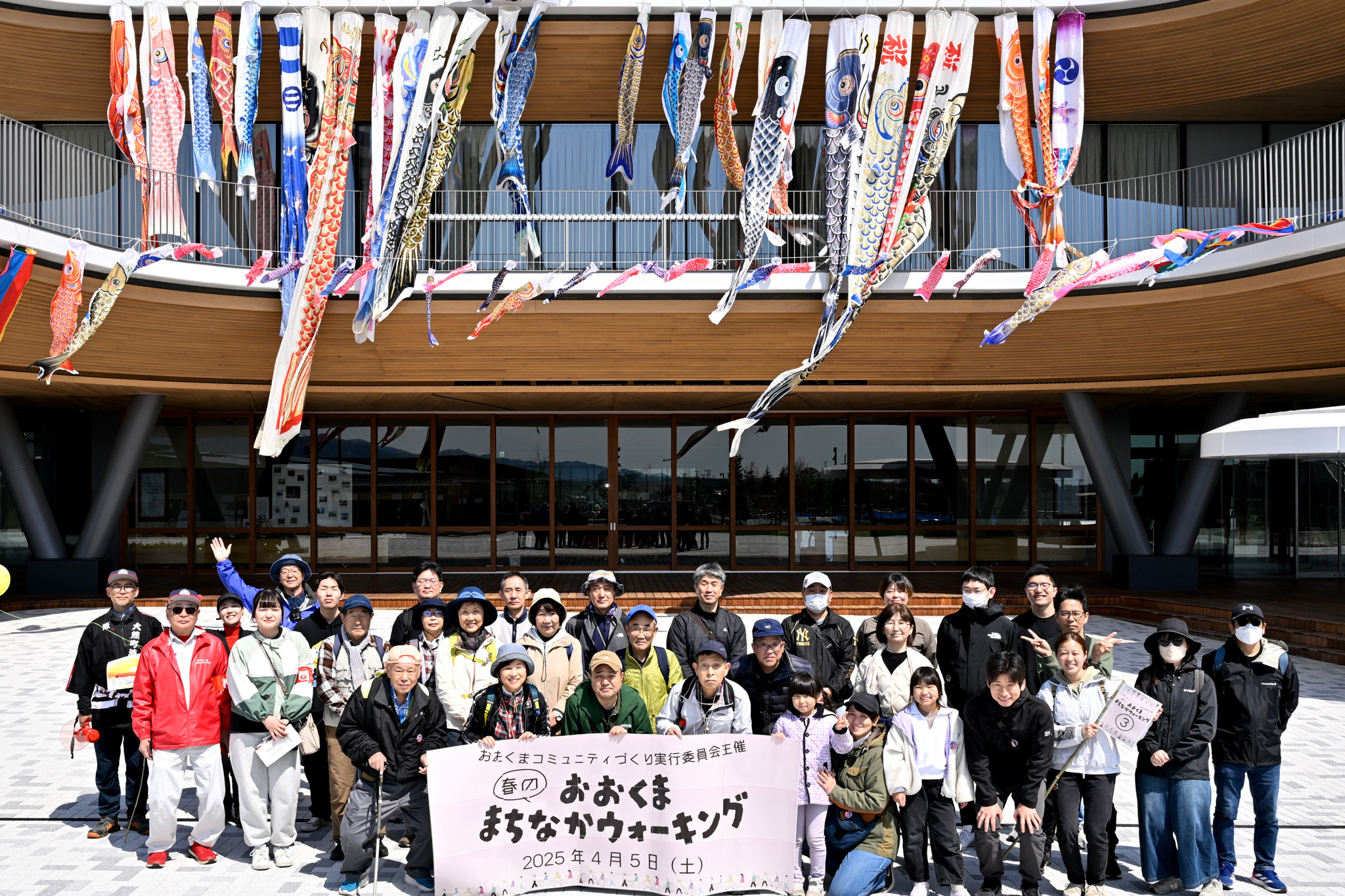 参加者は3班に分かれ、新しい街並みを眺めながら春の大熊町を歩きました。写真はCREVAおおくまの正面エントランスで撮影した集合写真です。