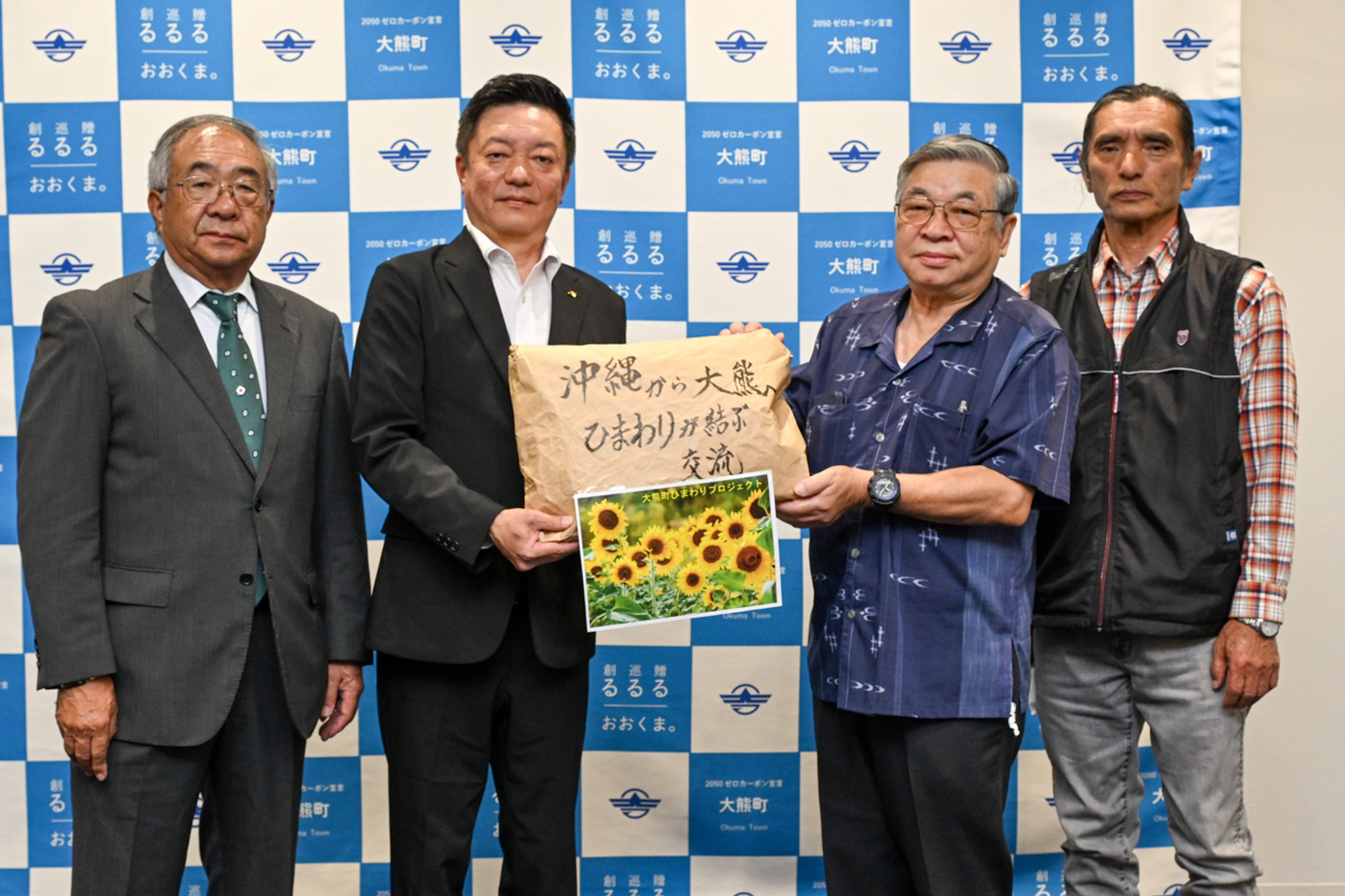鈴木副理事（右から2人目）から種を受け取る吉岡副町長