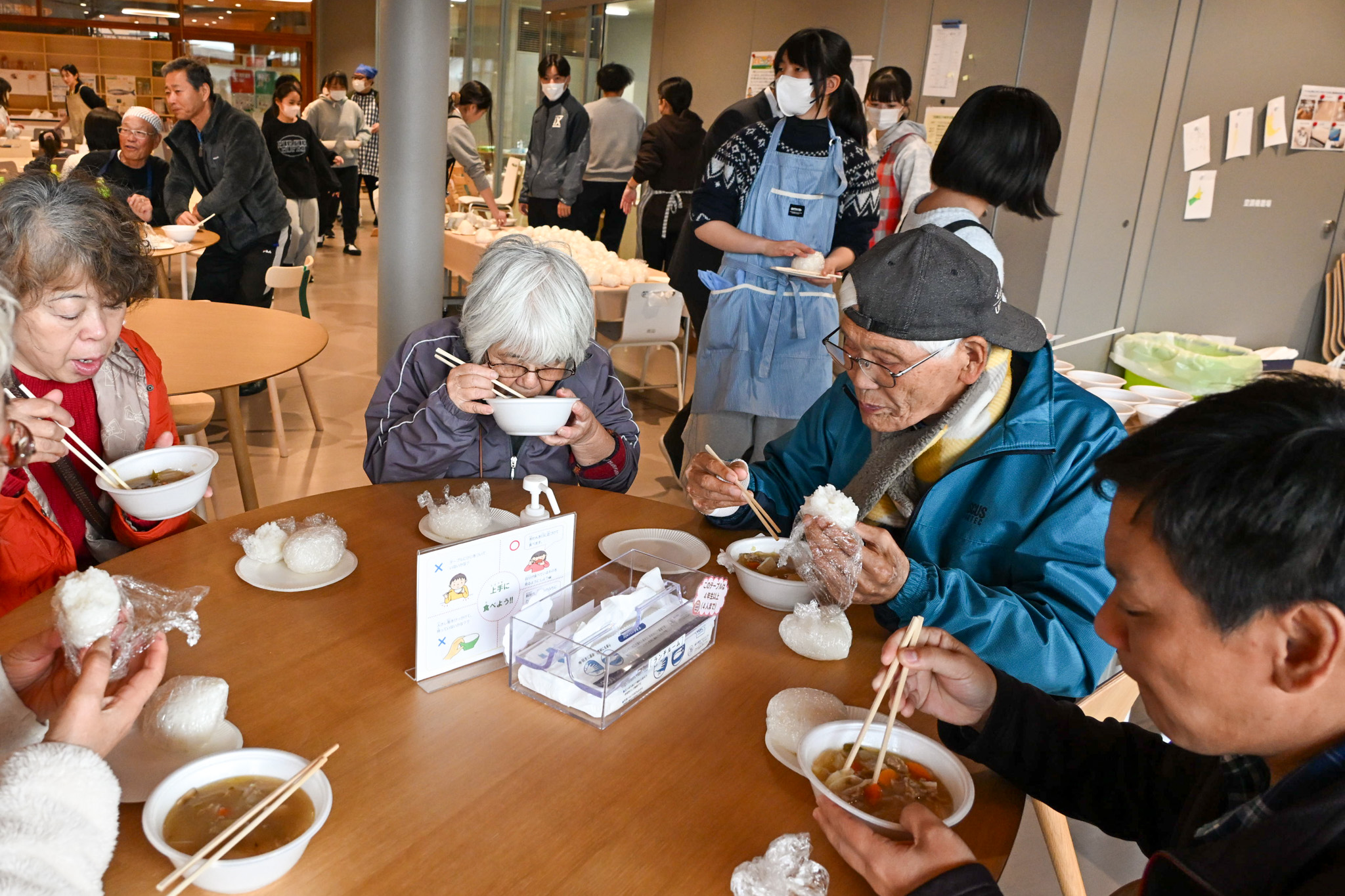 町立学び舎ゆめの森と町社会福祉協議会主催の芋煮会が、11月26日開かれました。地域の皆さんと子どもたちが交流を深め、つながりを育むために企画された催しです。写真は、子どもたちが手作りした豚汁と塩おにぎりを味わう参加者の様子です。