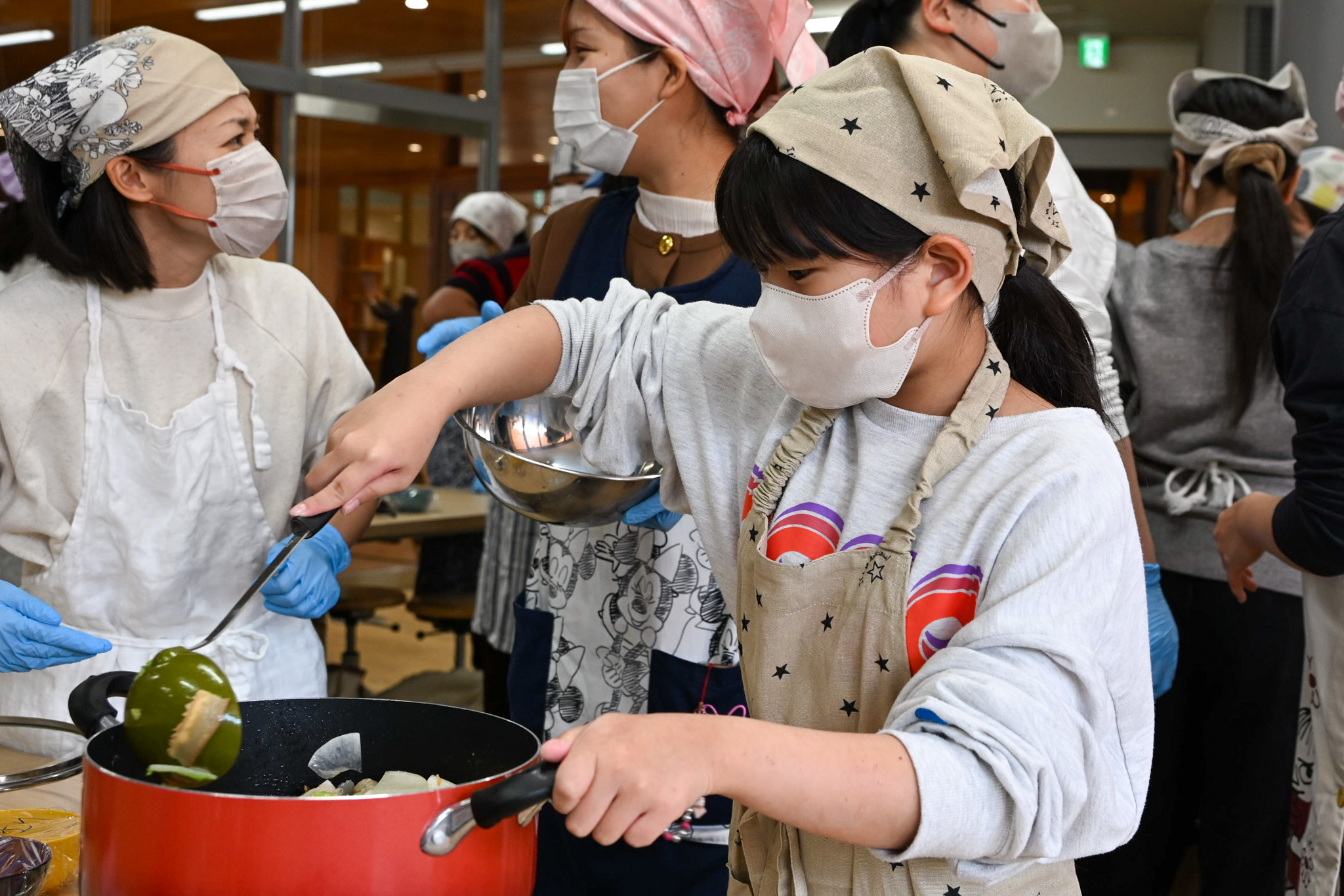 調理は5～9年生の児童生徒が担当し、下ごしらえにはボランティアの皆さんが協力しました。写真は、野菜を鍋で炒めている様子です。