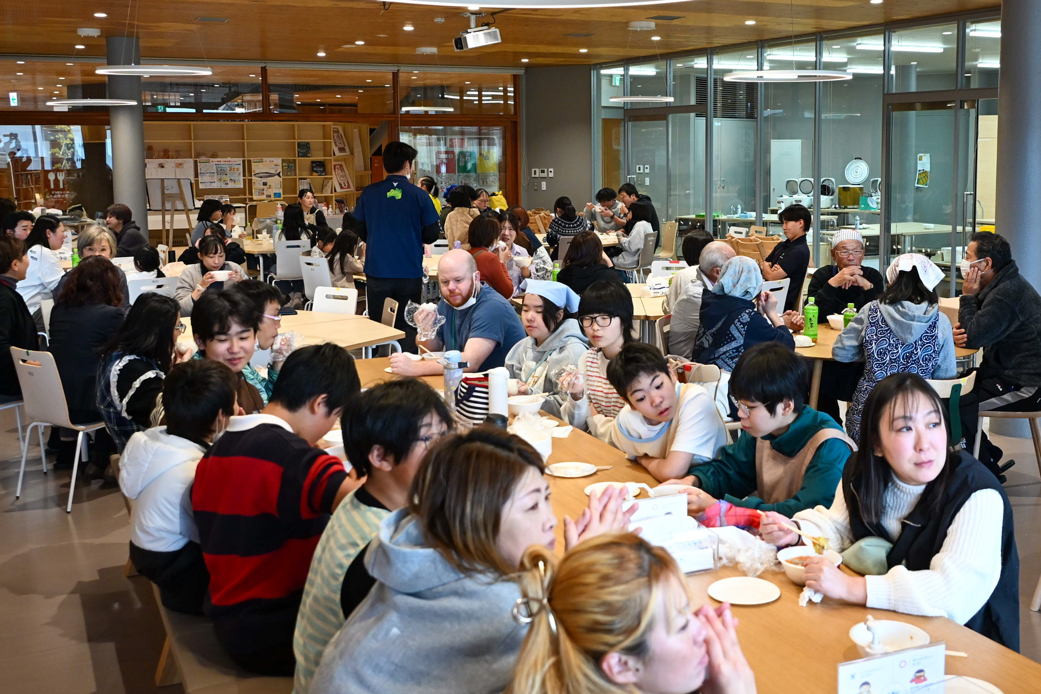 写真はランチルームの様子です。地域の皆さんや保護者の方々が、子どもたちが作ったできたての料理を囲み、和やかに過ごしています。