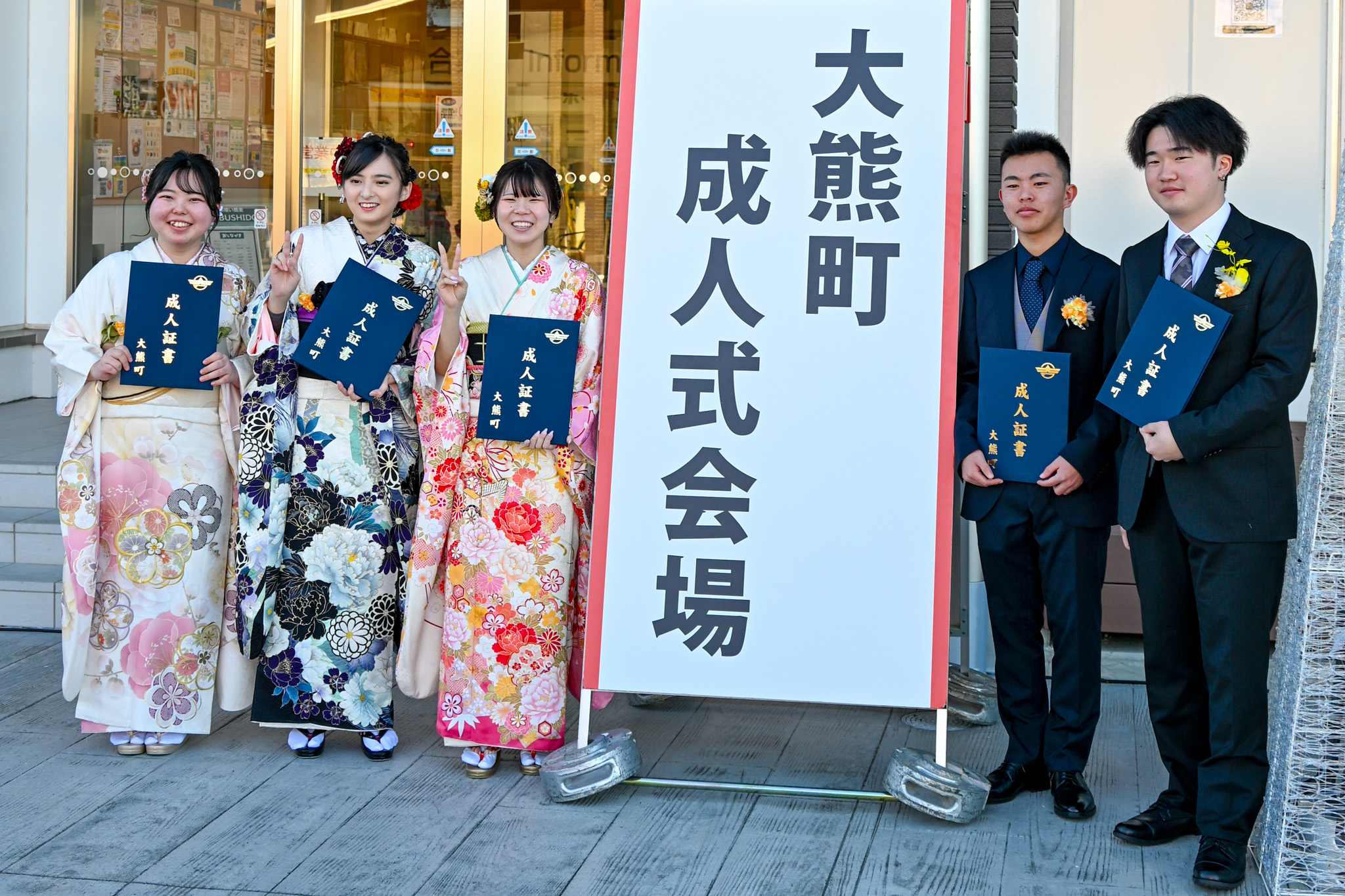 成人式後、会場入口の看板を挟んで並び、撮影に応じる新成人の皆さん。