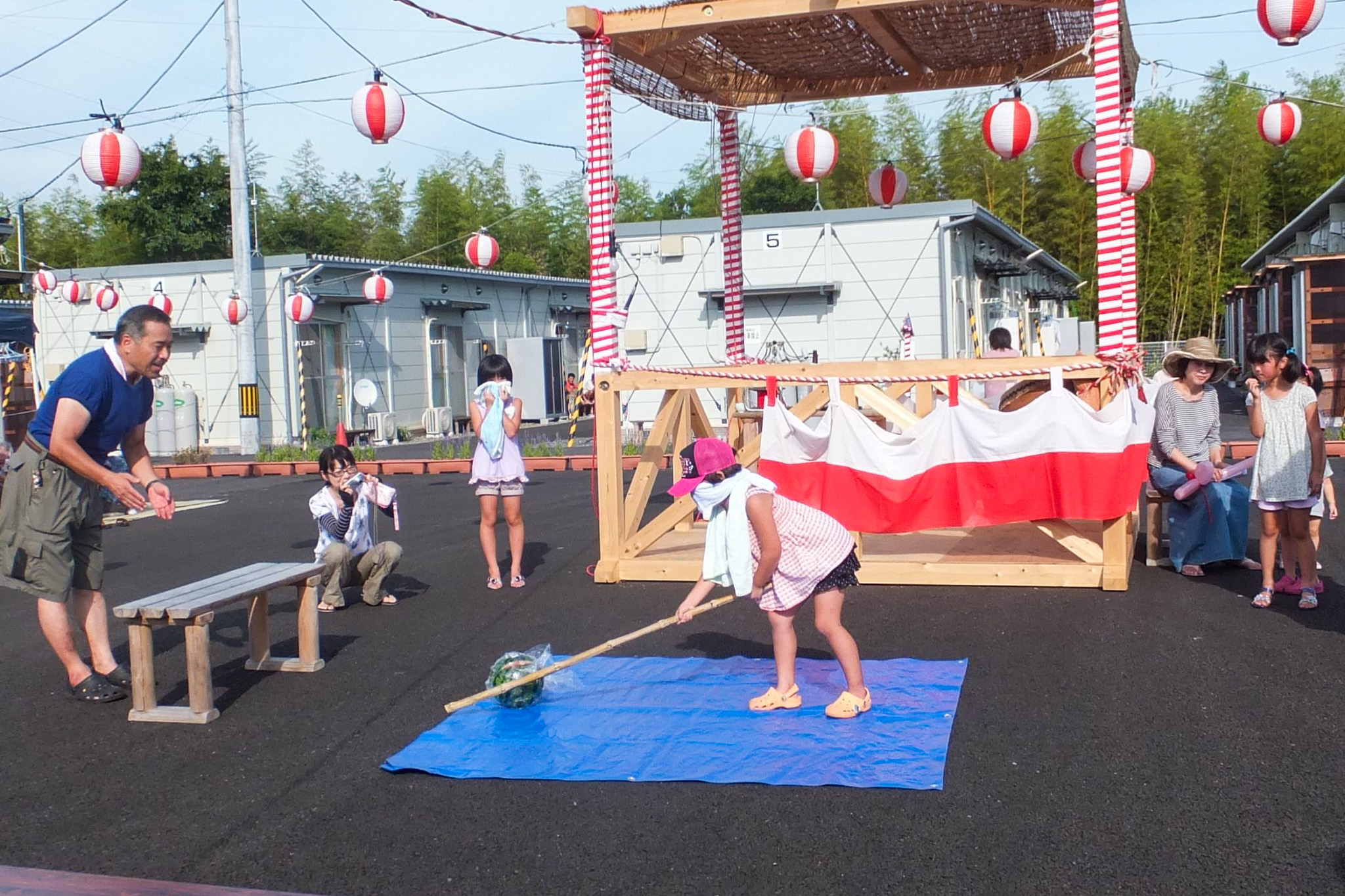 目隠しした子どもがスイカめがけて棒を振る夏まつり会場の様子