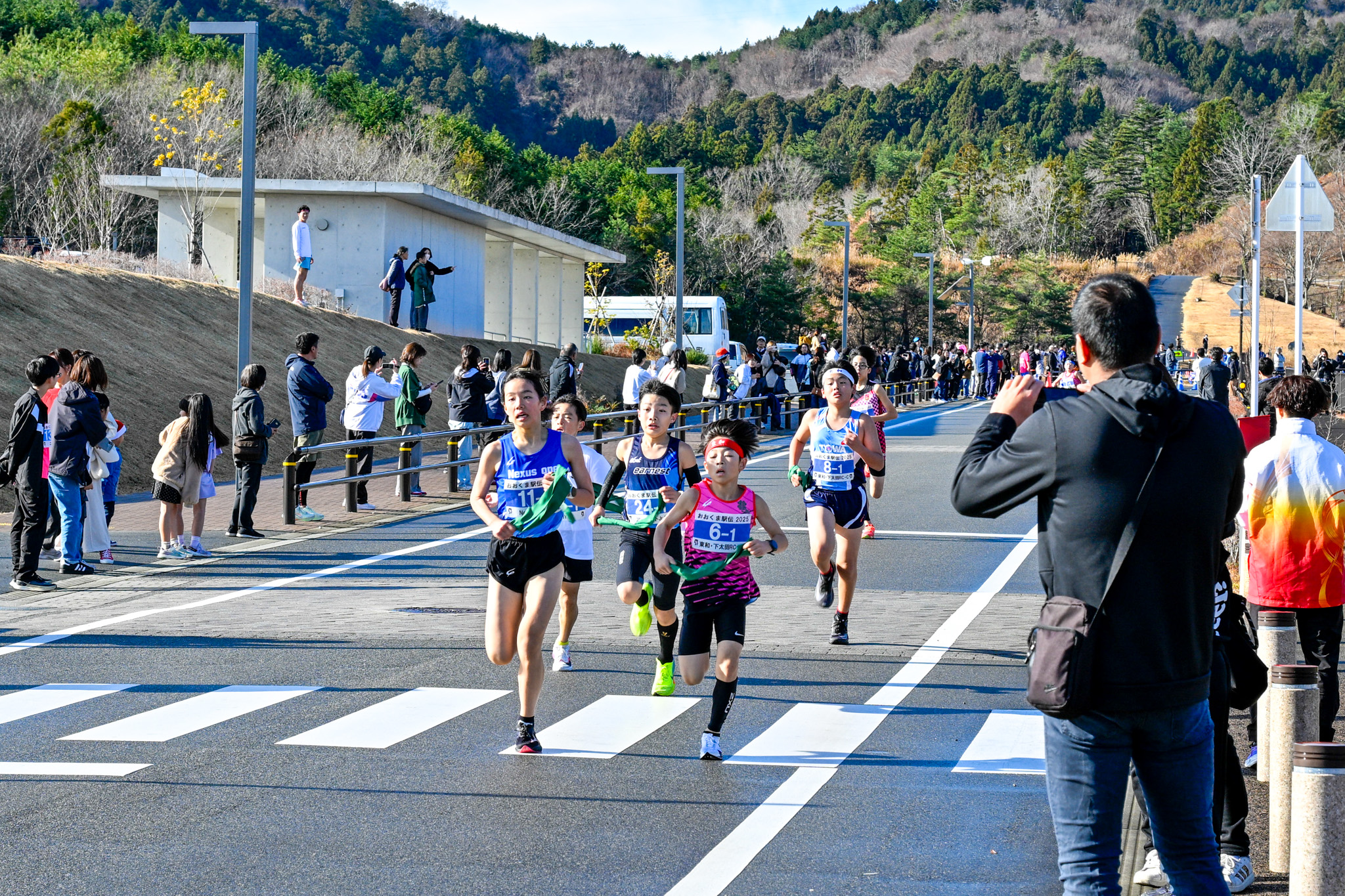 走りが進むにつれて集団が小さく分かれ、沿道には家族や友人の声援を受けながら、選手たちがタスキを手に中継地点を目指して走っています。