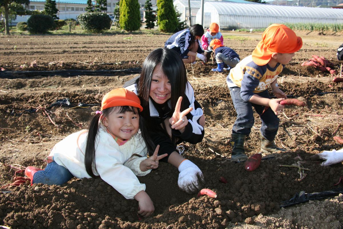 サツマイモを掘りながら嬉しそうにポーズをとる園児と双葉翔陽高校生