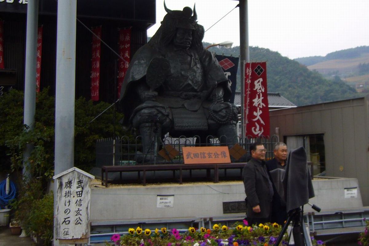 武田信玄公像の前に立ち記念撮影をする参加者