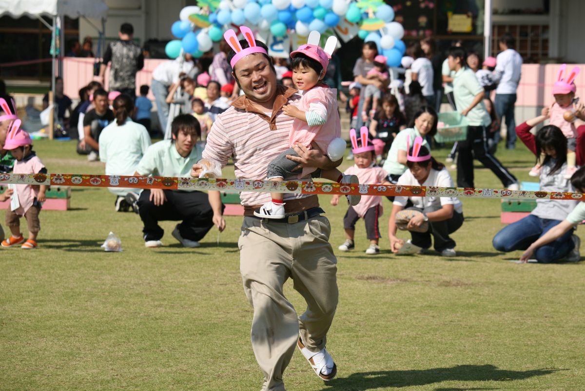 ウサギの長い耳としっぽを付け、お父さんに抱っこされて笑顔でゴール