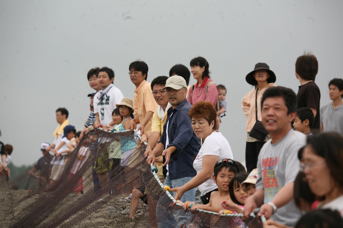 毎年恒例の地引き網で力いっぱい網を引く海水浴客