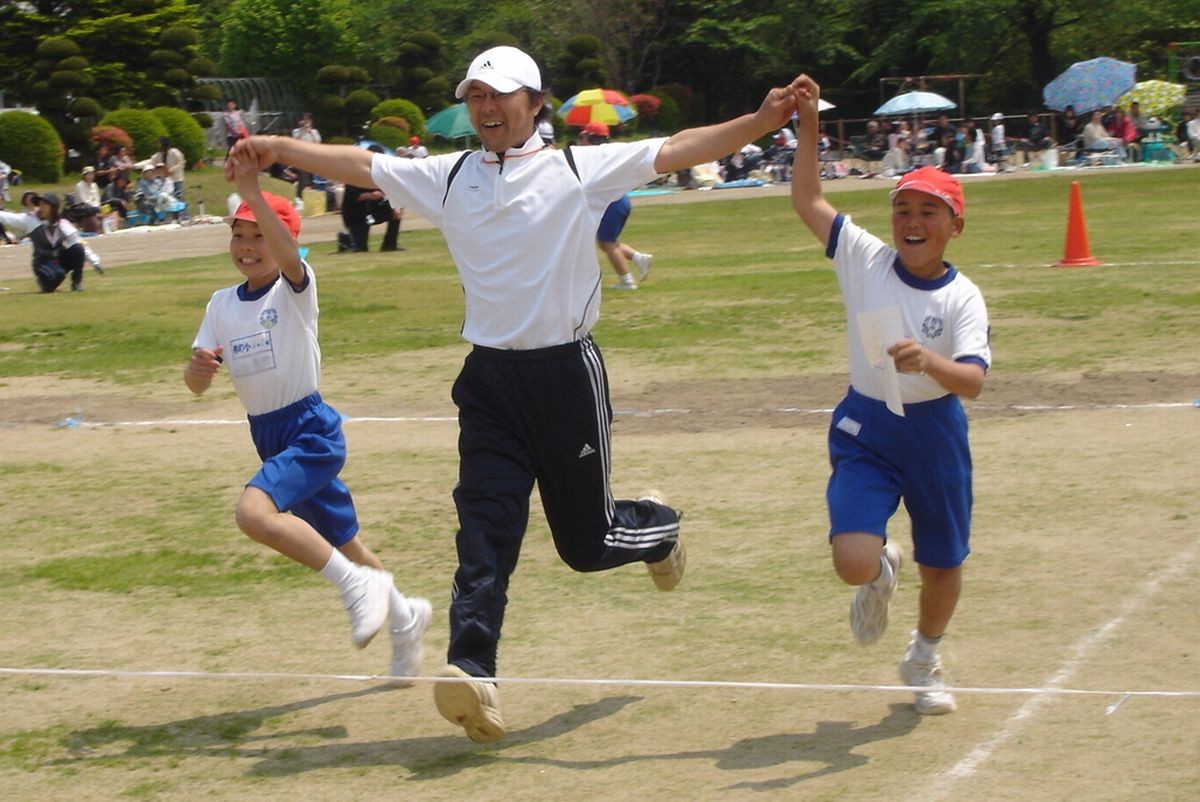 「先生と一緒」先生と手をつなぎ万歳をしながら1位でゴールテープを切る6年生