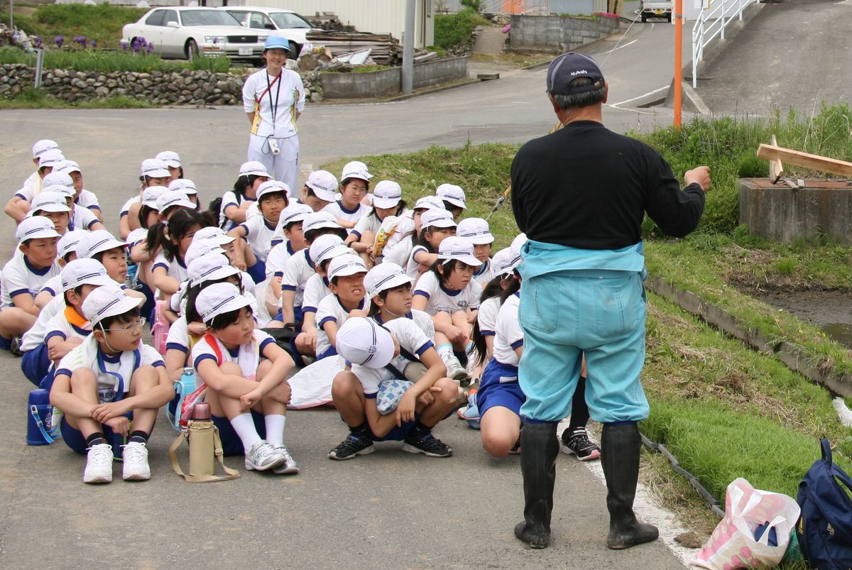 田植えを体験する前に農家の方の説明を聞く児童たち