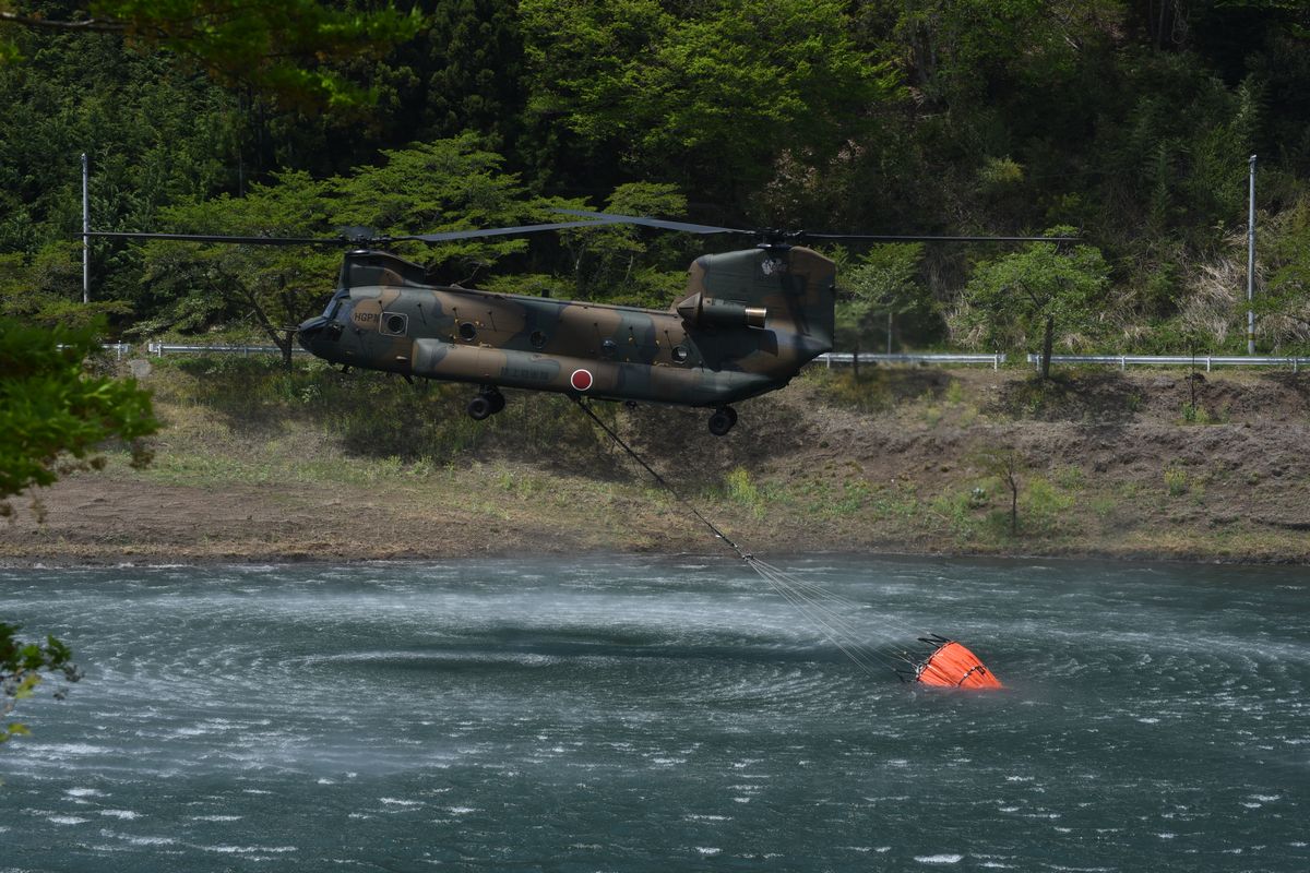 機体に吊り下げた空中消火用バケツにダム湖の水を補給するヘリコプター