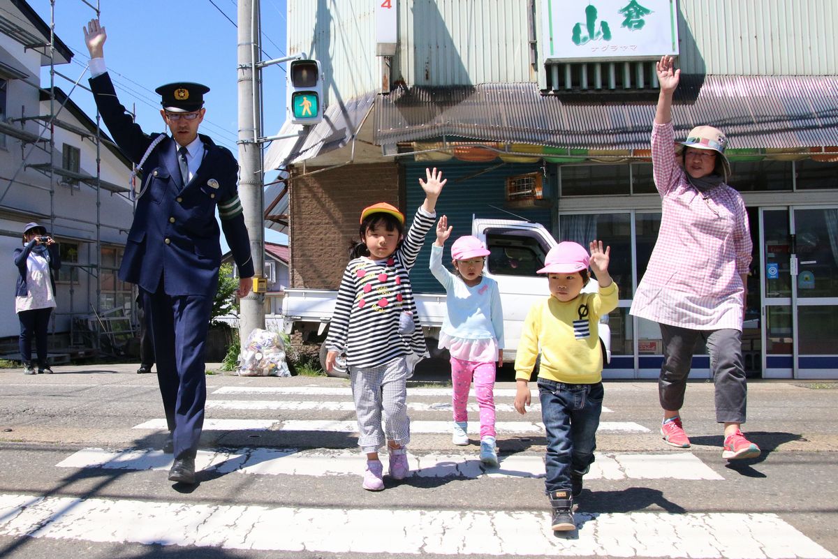 しっかりと手を上げて、警察官、先生と横断歩道を渡る園児