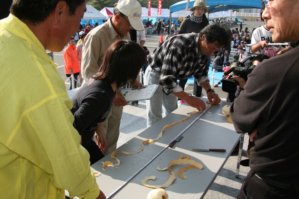「大熊梨皮むき大会」で参加者が剥いた皮の長さをメジャーで測る審査員