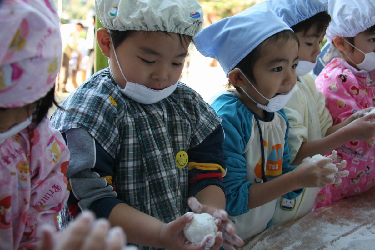 手に粉をつけてついた餅を食べやすい大きさにちぎり、丸く整える園児たち